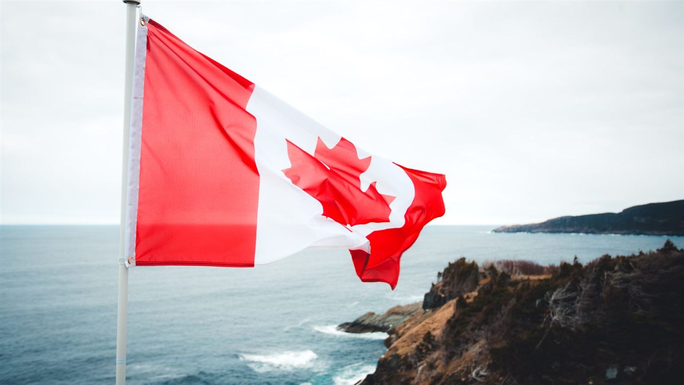 Canadian flag waving over a rugged coastline